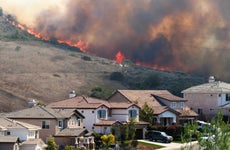 A suburban neighborhood near a hill with a wildfire in the background.