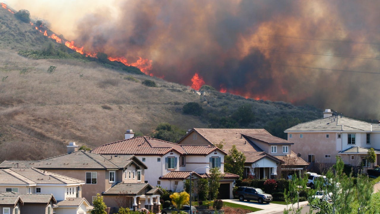 A suburban neighborhood near a hill with a wildfire in the background.