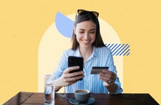 woman holding a credit card and phone in her hands while sitting down with coffee and a glass of water in front of her