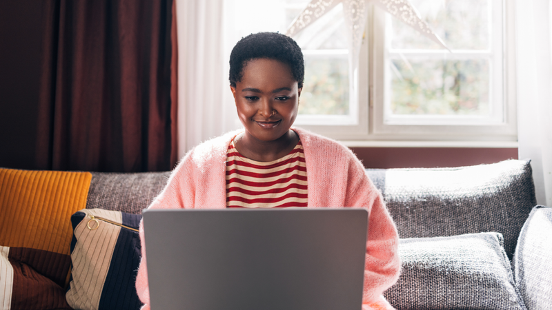 An Afro-American woman sitting on the couch in the living room, spending her Christmas holidays watching a movie on her computer.