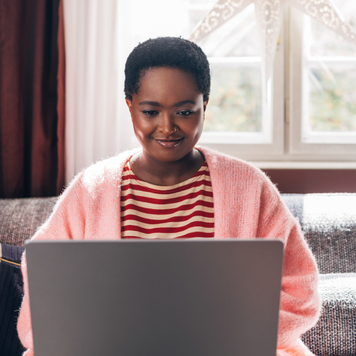 An Afro-American woman sitting on the couch in the living room, spending her Christmas holidays watching a movie on her computer.