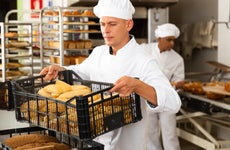 Male baker carrying a crate with baked bread in his bakery.