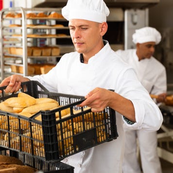 Male baker carrying a crate with baked bread in his bakery.