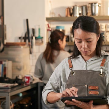 A cafe owner in coffee shop and wearing an apron holds a digital tablet.