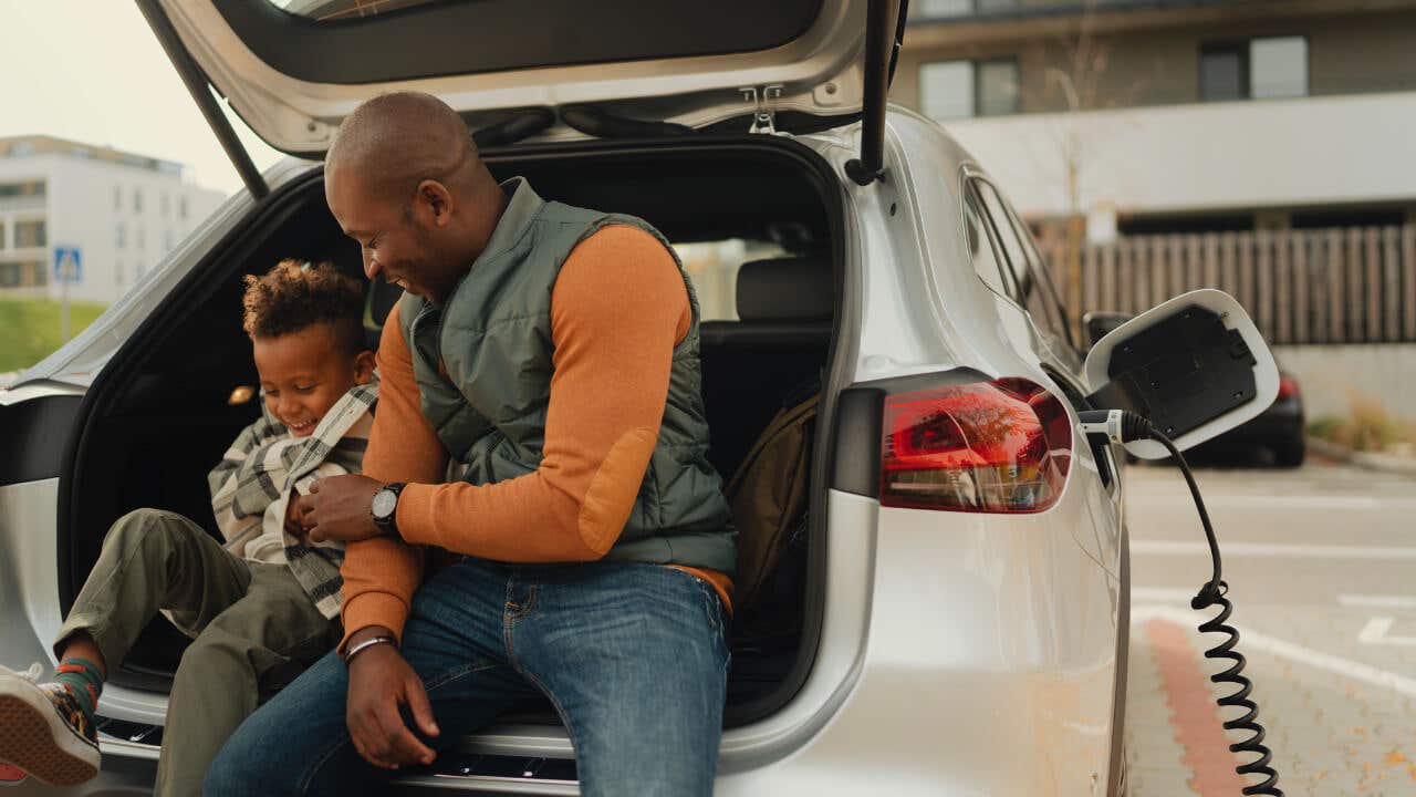 A black father and his child sit in an electric car while it charges.