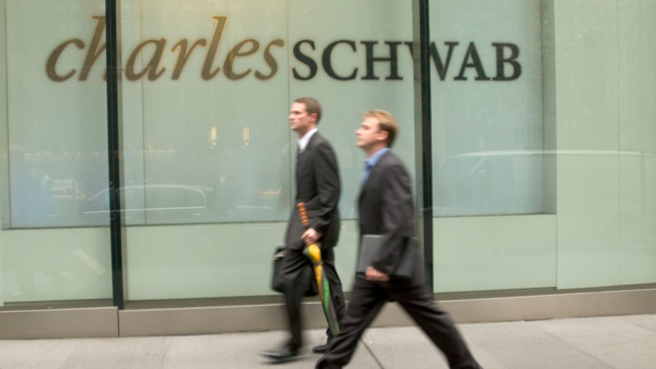 Two businessmen walk by a Charles Schwab building