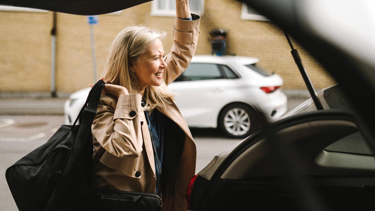 A white, older businesswoman closes the trunk of her car.