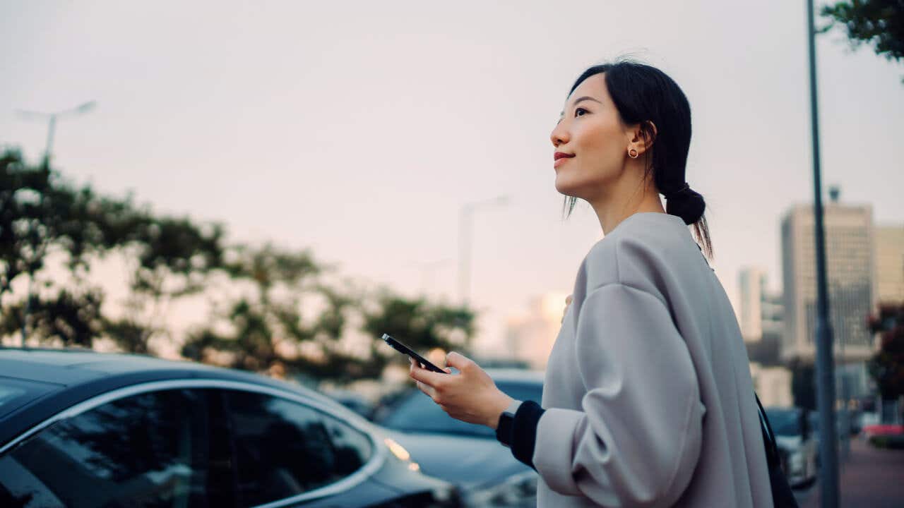 A young Asian woman holds her phone near her car