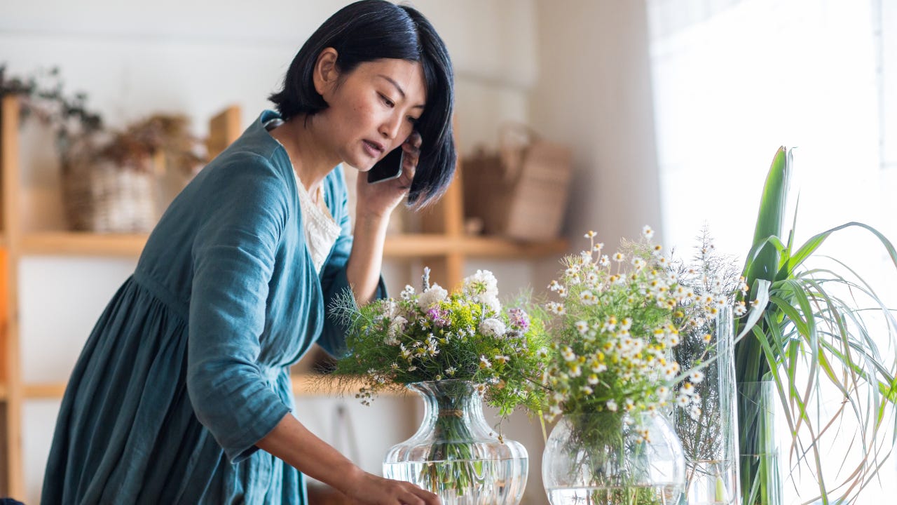 A florist talks on her cellphone while arranging flowers in vases.