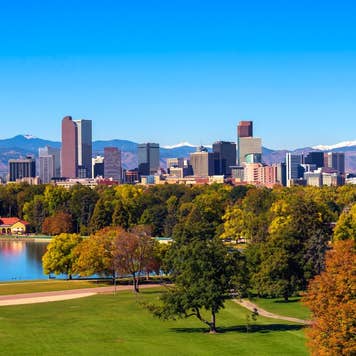 City skyline of Denver Colorado downtown with snowy Rocky Mountains and the City Park Lake.
