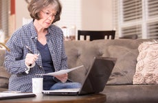 Older woman reviews financial documents and has a laptop.