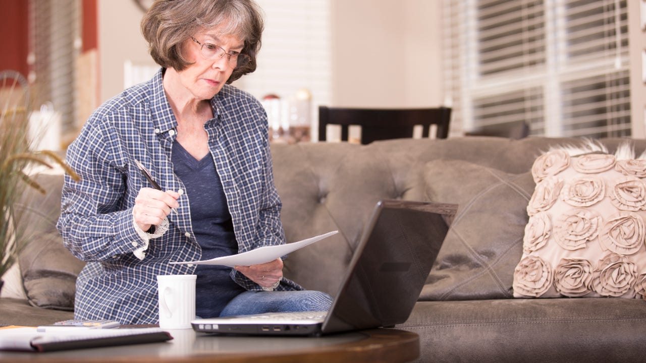 Older woman reviews financial documents and has a laptop.
