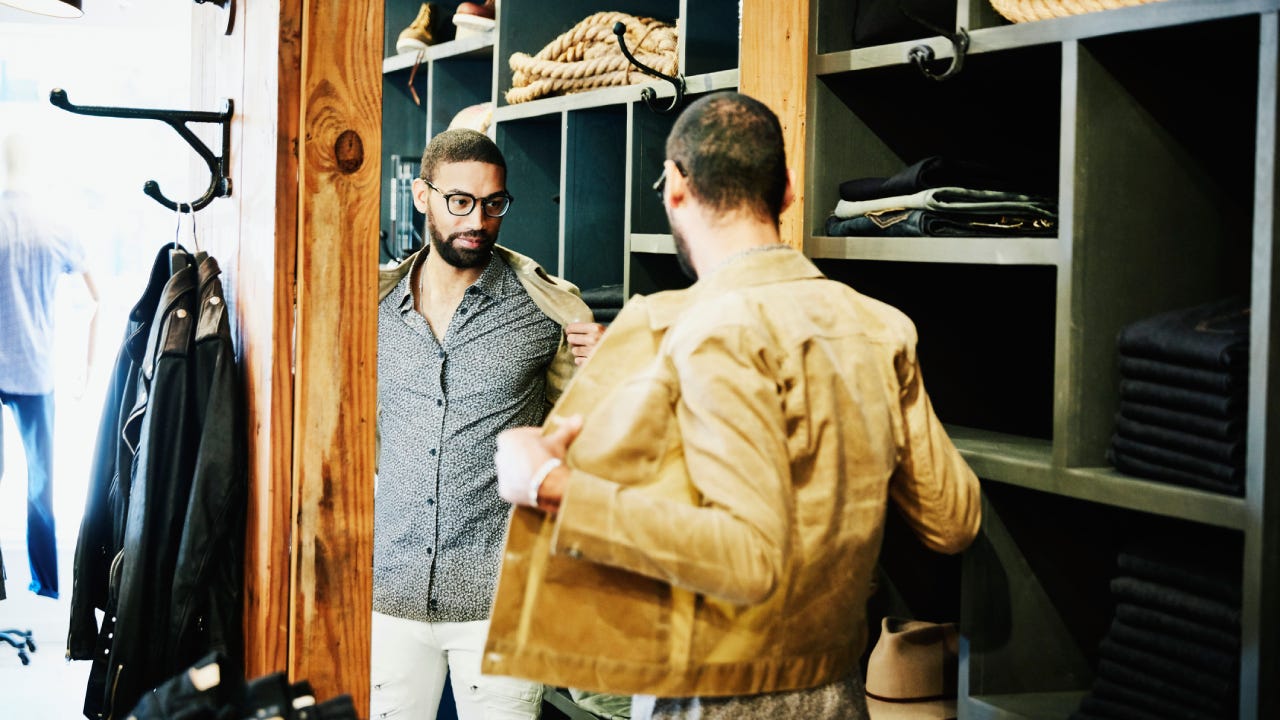 Man trying on jacket while looking in the mirror in mens clothing shop