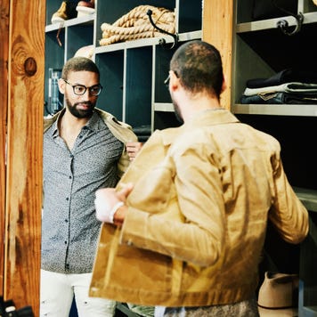 Man trying on jacket while looking in the mirror in mens clothing shop