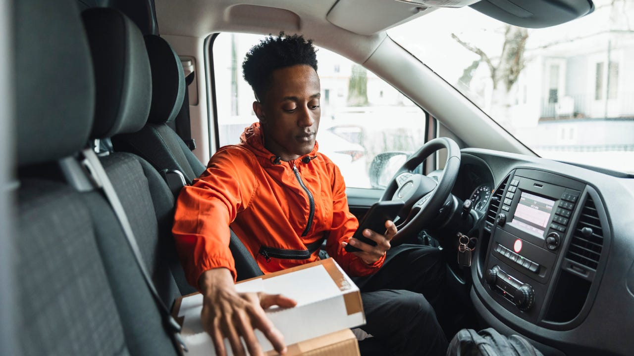 Young male driver using smart phone while sitting in delivery van