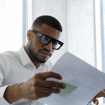 A small business owner sits in his office, looking over papers and working on his laptop.