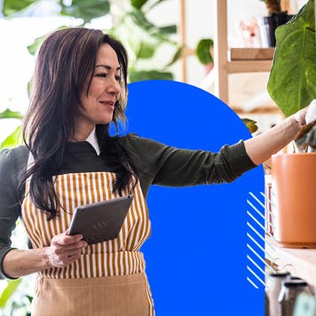 A shop owner in a striped apron holds a tablet.