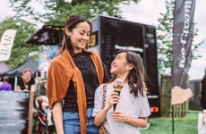 Lovely girl enjoying ice cream with her young pretty mom in front of a food truck at food festival