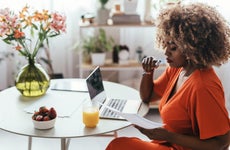 Black female entrepreneur working from home, sitting at the kitchen table and analyzing a report on her computer.
