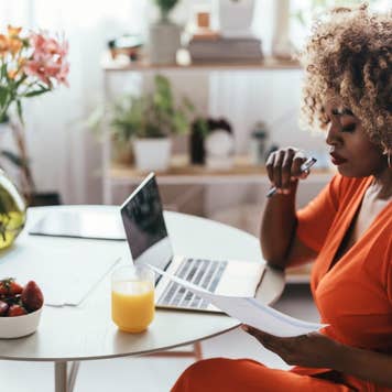 Black female entrepreneur working from home, sitting at the kitchen table and analyzing a report on her computer.