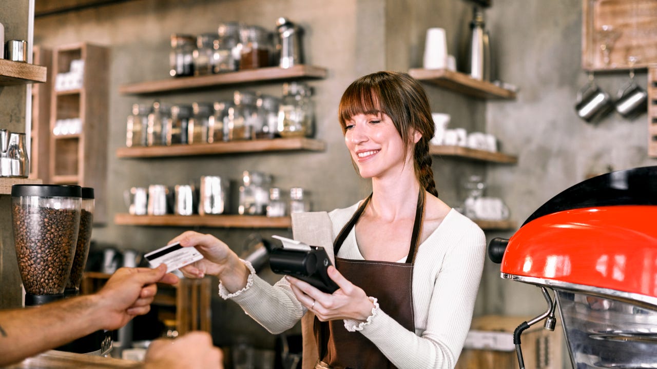 A coffee shop owner takes a customer’s credit card.