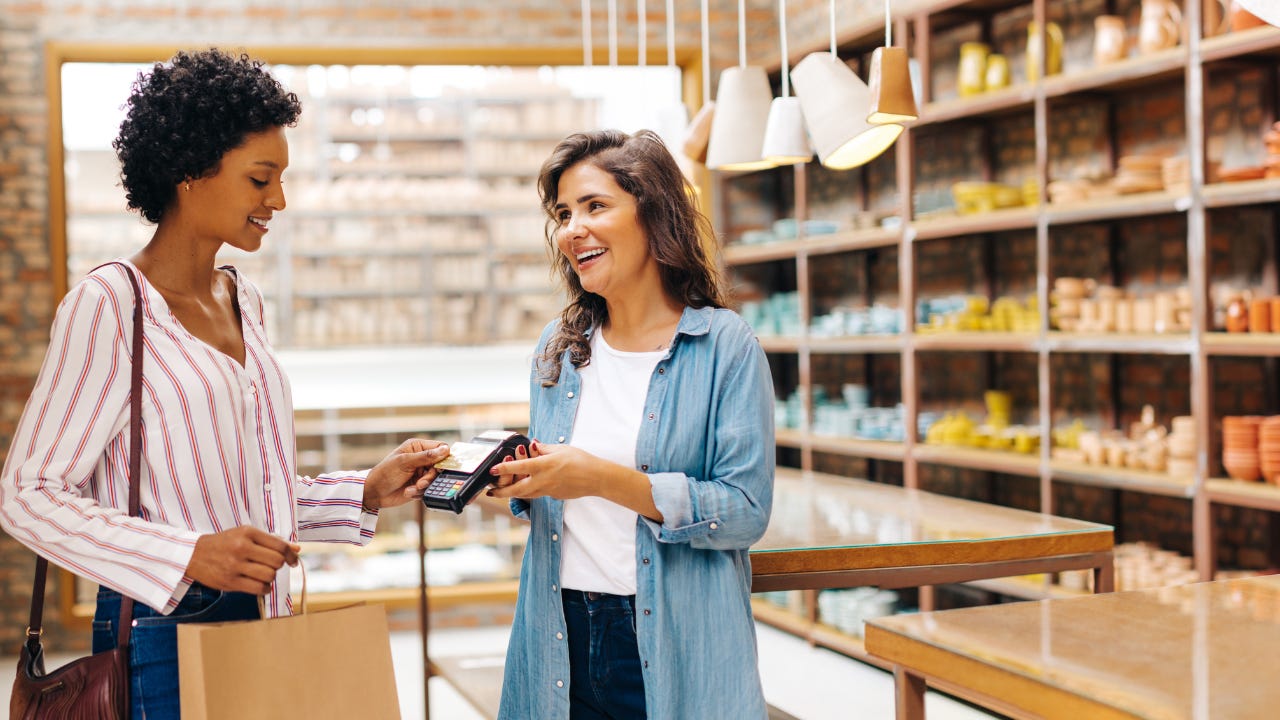 A smiling shop owner receives a contactless credit card payment from a happy customer.