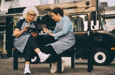 Two women review a table and notes while sitting outside a food truck.