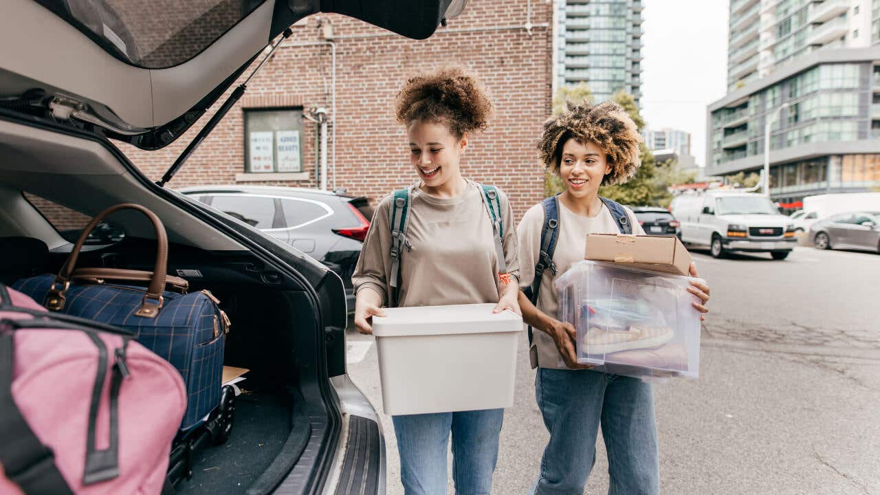 Two Black college students load boxes into the trunk of a car.
