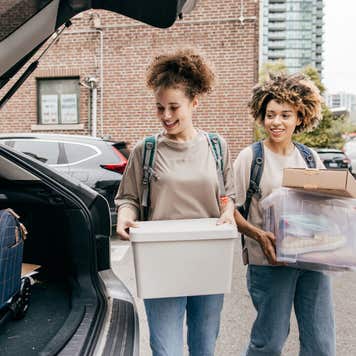 Two Black college students load boxes into the trunk of a car.