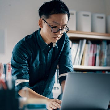 A man with glasses reviews notes on his computer at his office.