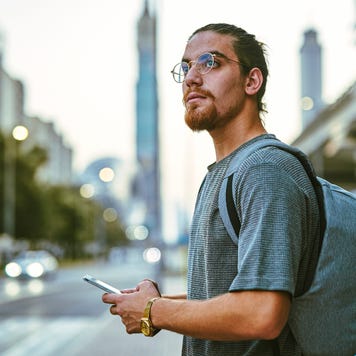 young man standing alone in the city and looking contemplative while using his cellphone