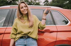 Smiling young woman with key standing in front of car