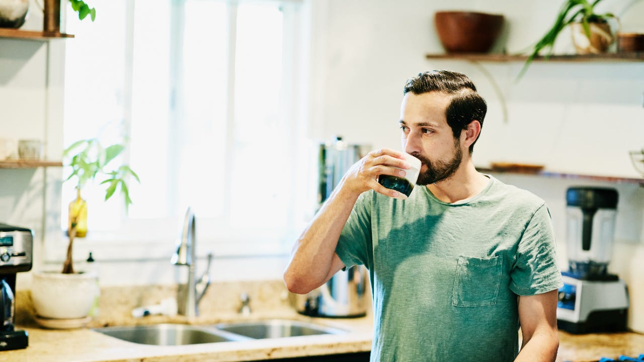 Person in a green shirt drinking coffee in his kitchen