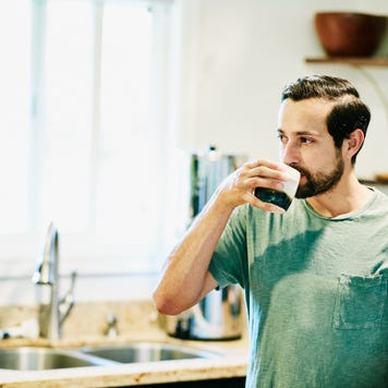 Person in a green shirt drinking coffee in his kitchen