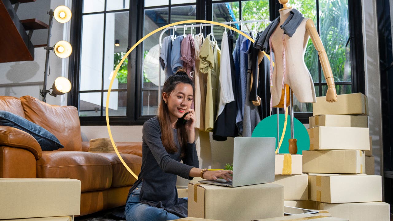 A woman working in front of a clothing rack and laptop.