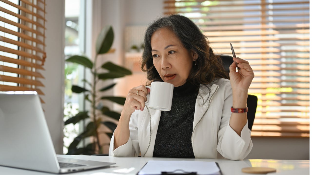 Professional elderly business woman looks stylish sip coffee during working with laptop.