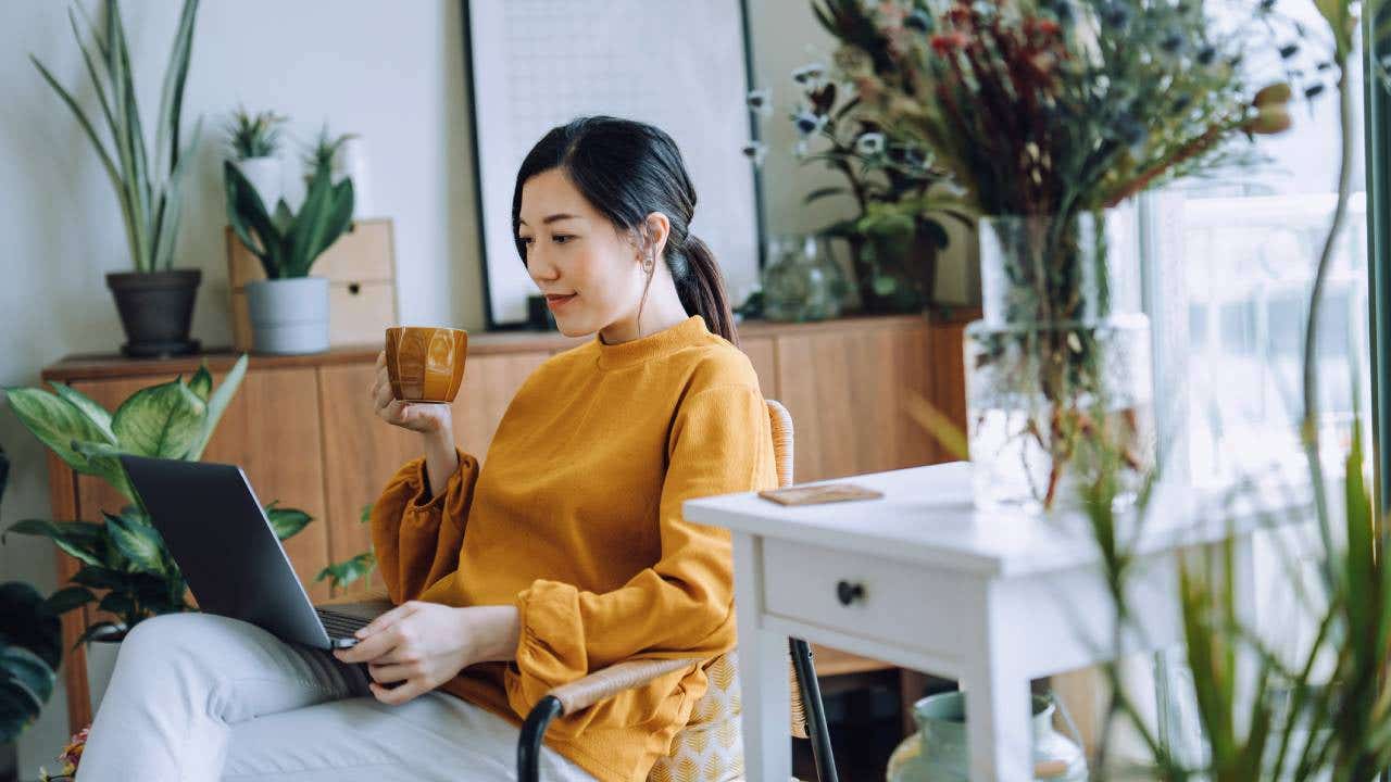 woman sitting on armchair using laptop while relaxing in living room at home