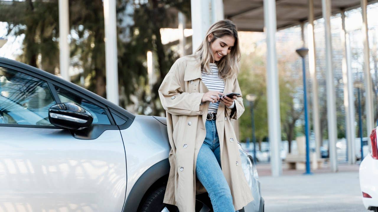 Young blond woman using smartphone, leaning on a car