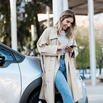 Young blond woman using smartphone, leaning on a car