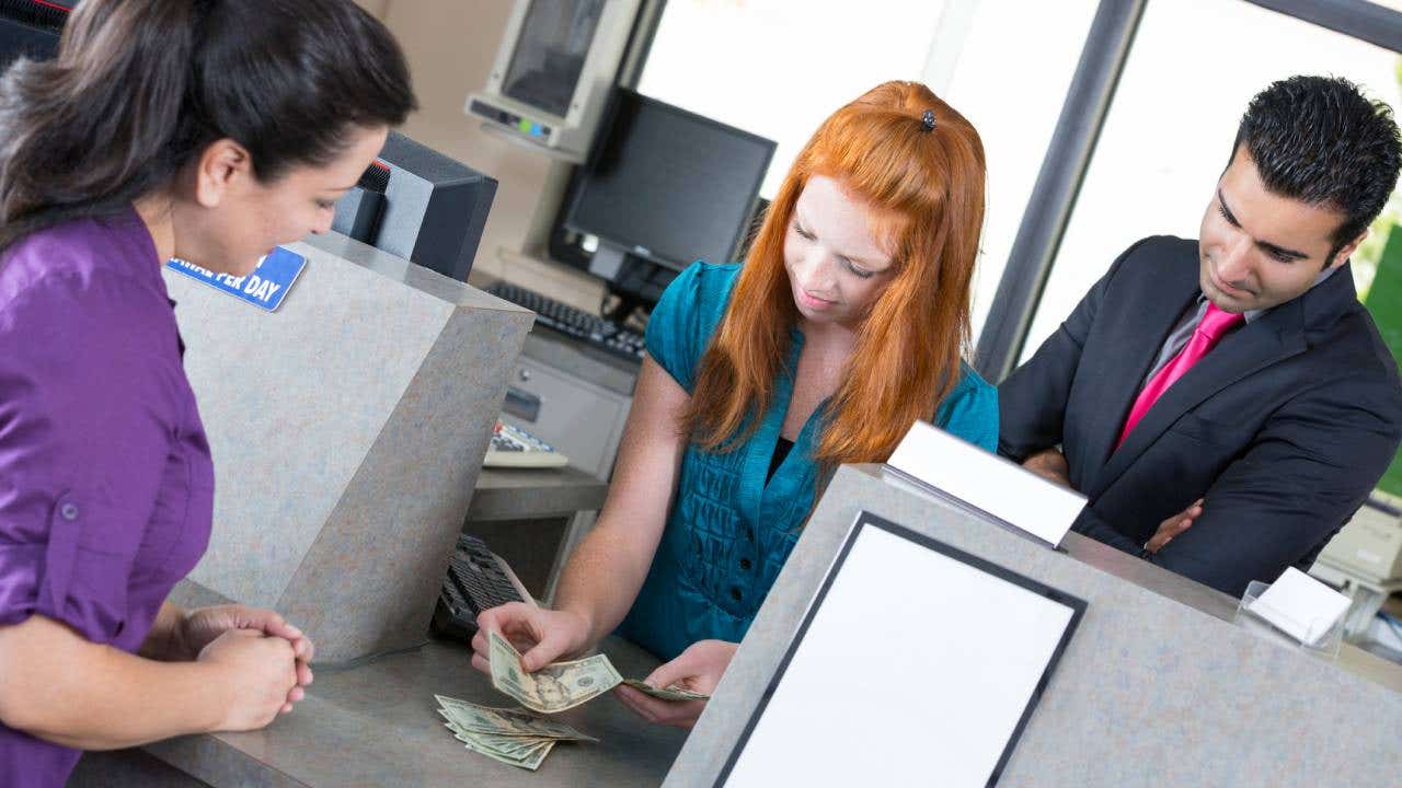 Young bank teller counting money as her supervisor watches