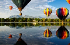 Colorful hot air balloons glide over Prospect Lake in Colorado Springs, CO, at the Colorado Balloon Classic; Cheyenne Mountain is in the background.