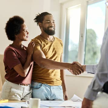 Happy black couple shaking hands with a homebuilder
