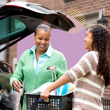 Young black woman handing plastic bin to older black woman to put basket into trunk of vehicle.