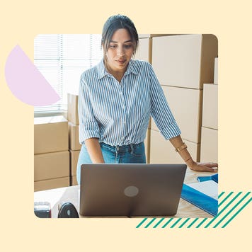 A small business owner stands while working on her laptop.