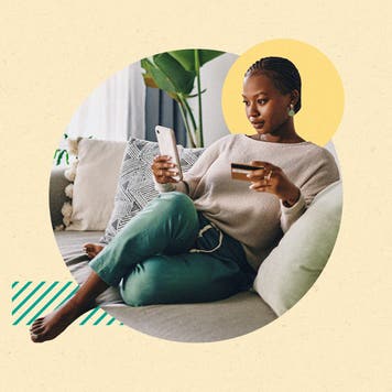 design image of a woman sitting on her couch and looking at a phone in her hand and a credit card in the other