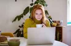 Woman drinking coffee and using laptop at home