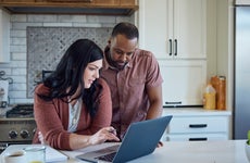Woman and man sit at kitchen counter with breakfast working with pen, paper and laptop