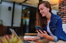 Young woman wearing white headphones using laptop and mobile phone for remote work