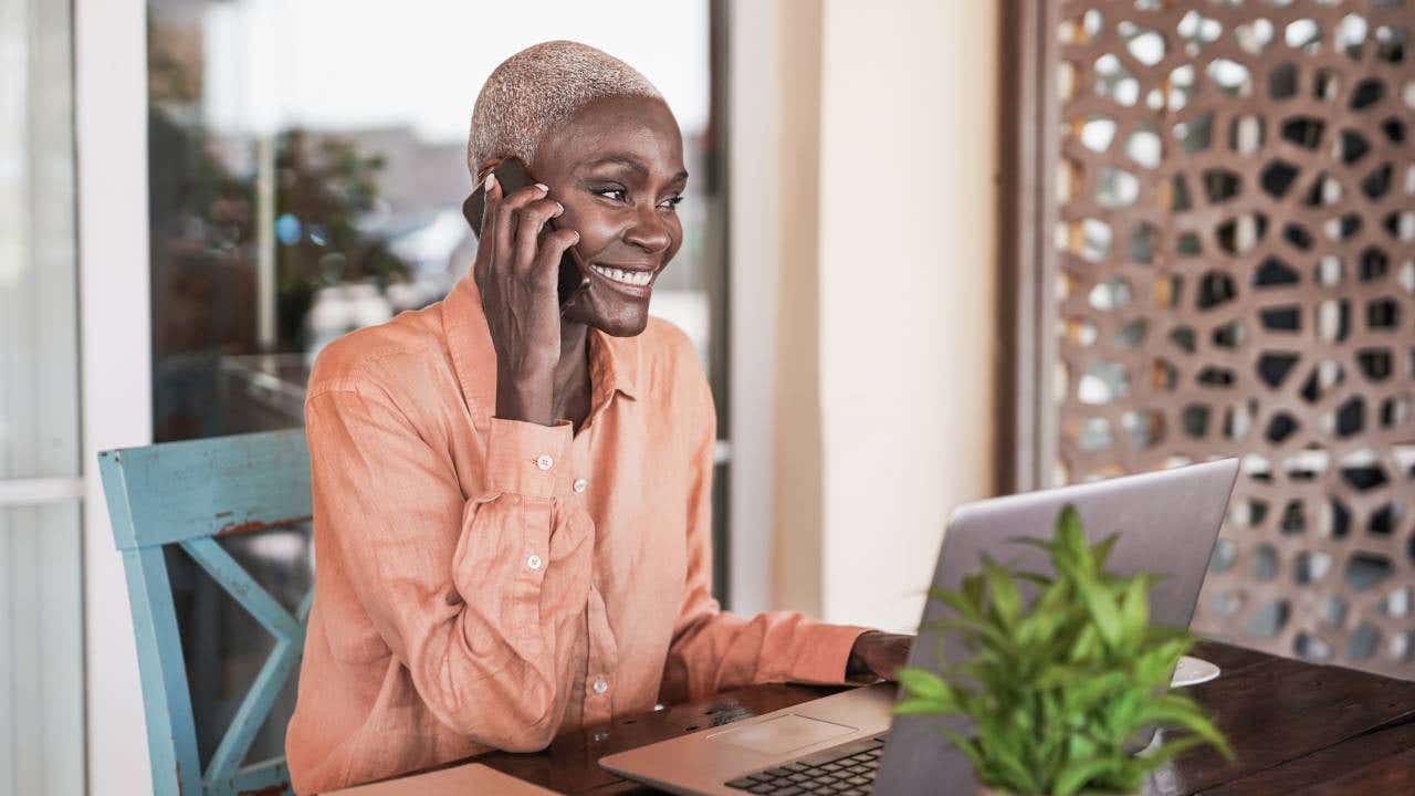 woman working with laptop outdoor while talking on smartphone call