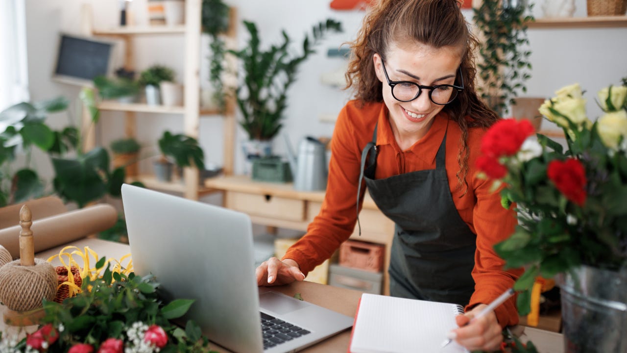 A florist/shop owner smiles as she works on a laptop